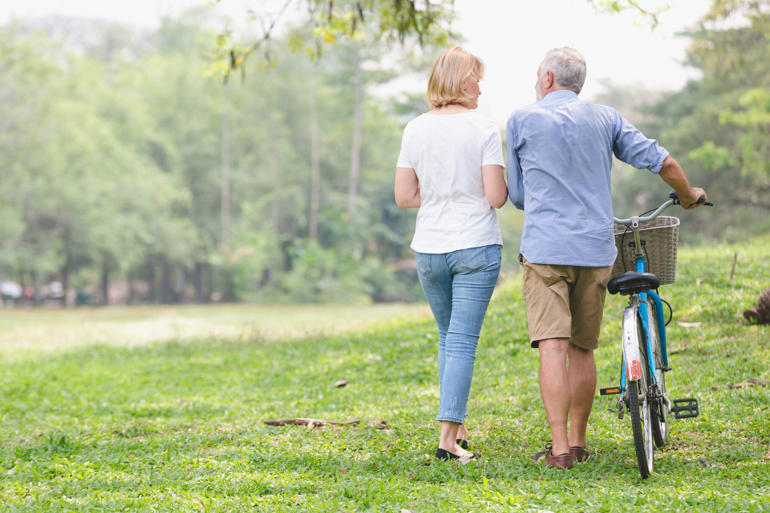 Senior couple walking their bike along happily talking happily.