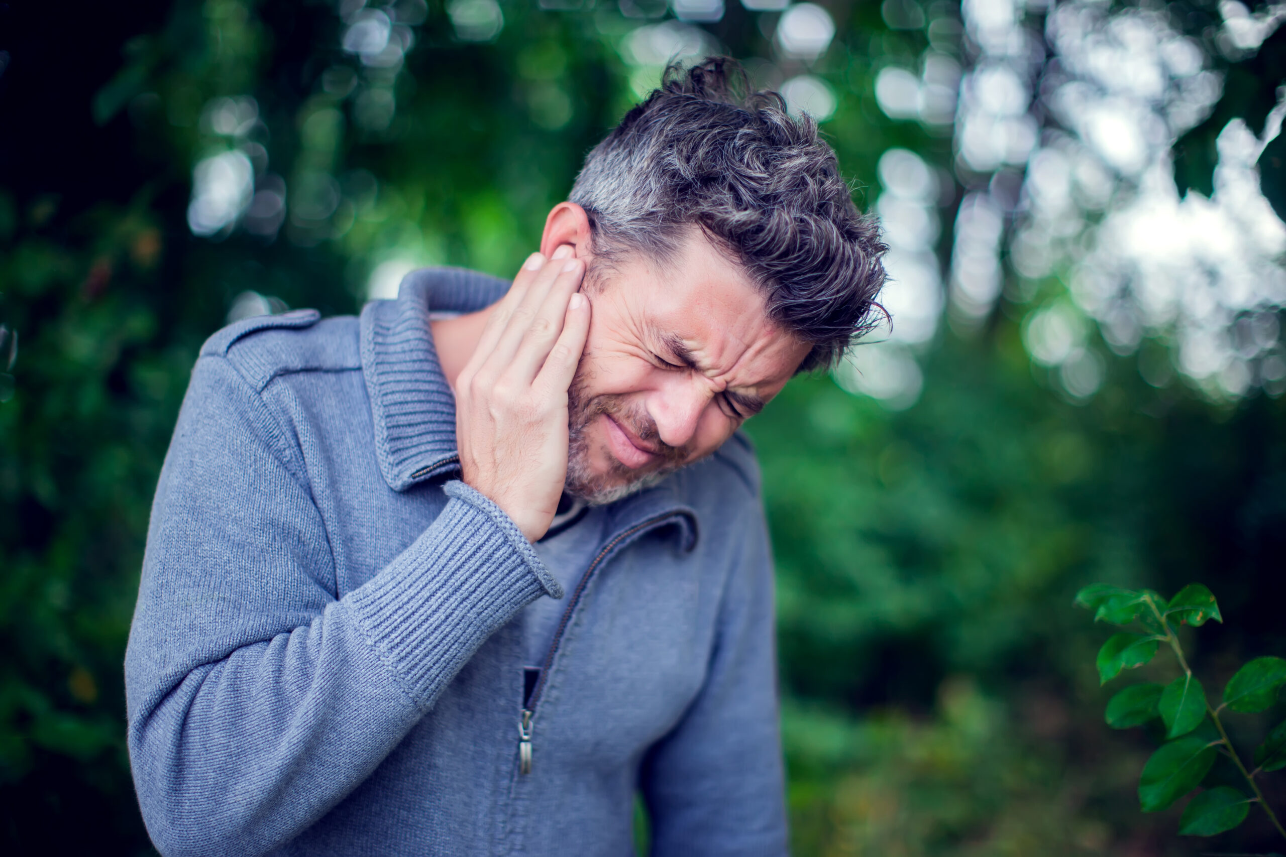 Unhappy male having ear pain touching his painful head outdoor