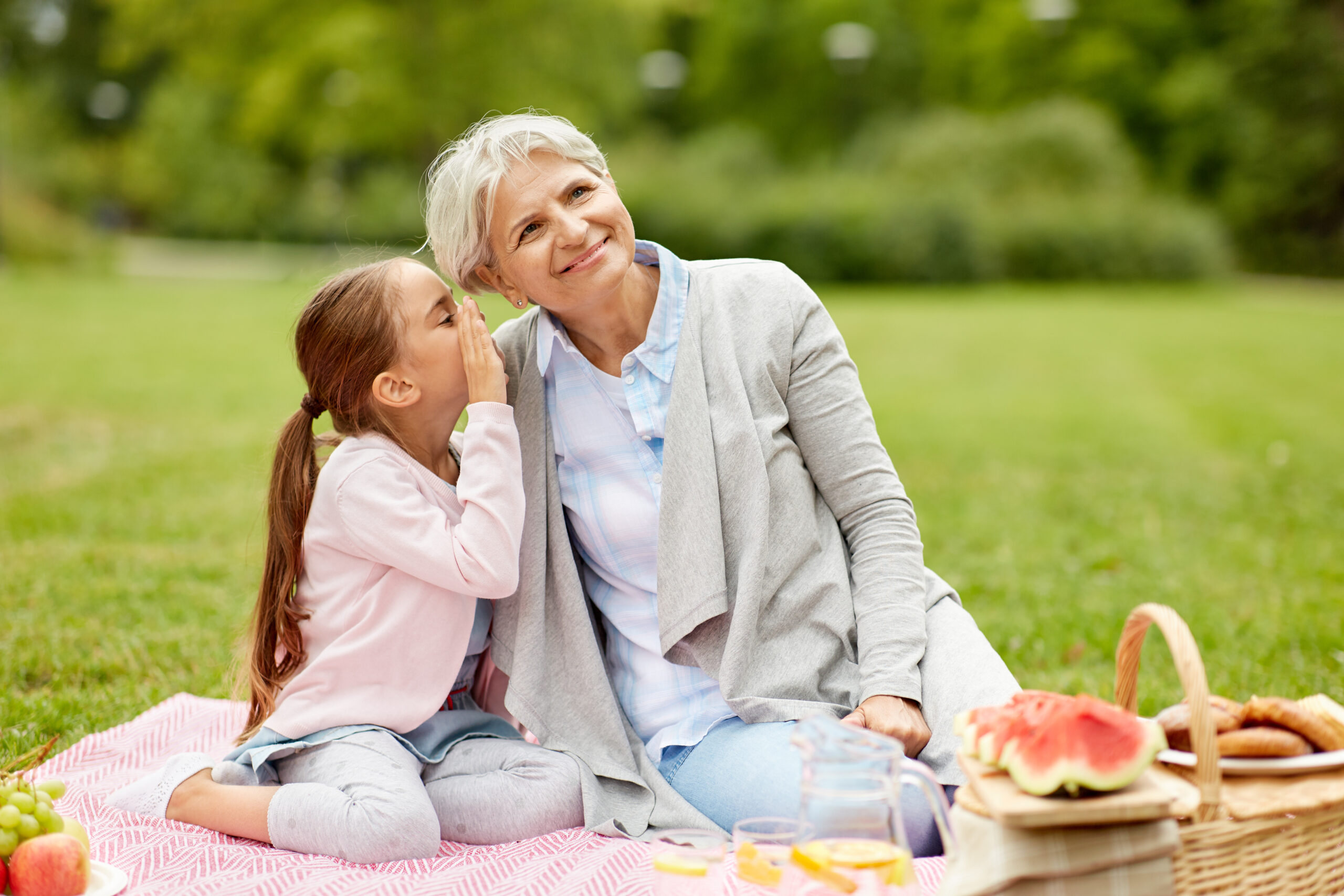 family, leisure and people concept - happy grandmother and granddaughter having picnic at summer park and sharing secrets