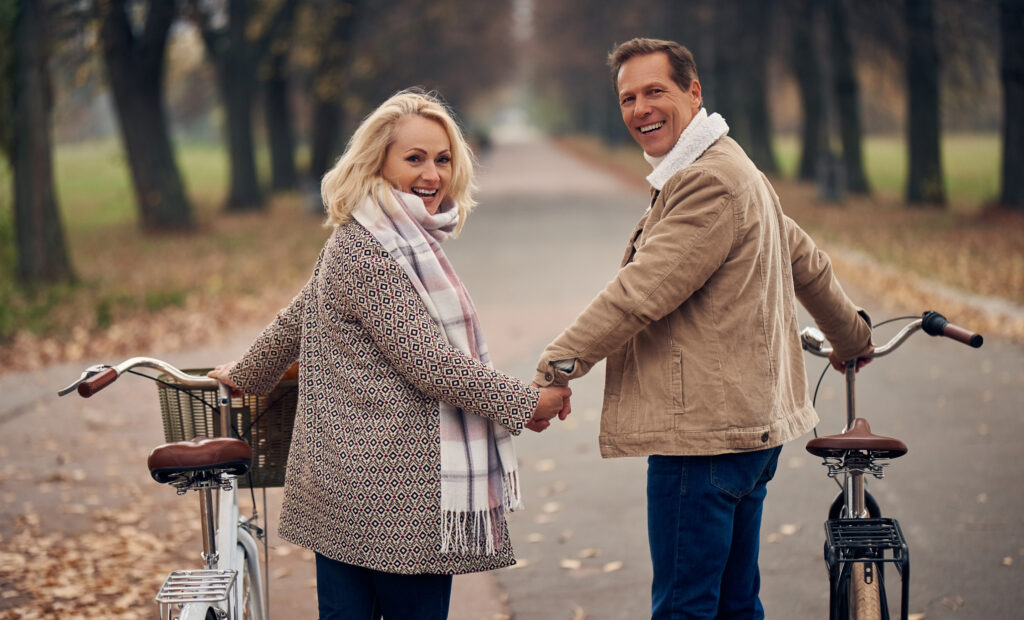 Senior couple walking in park in autumn. Attractive woman and handsome man spending time together with bicycles
