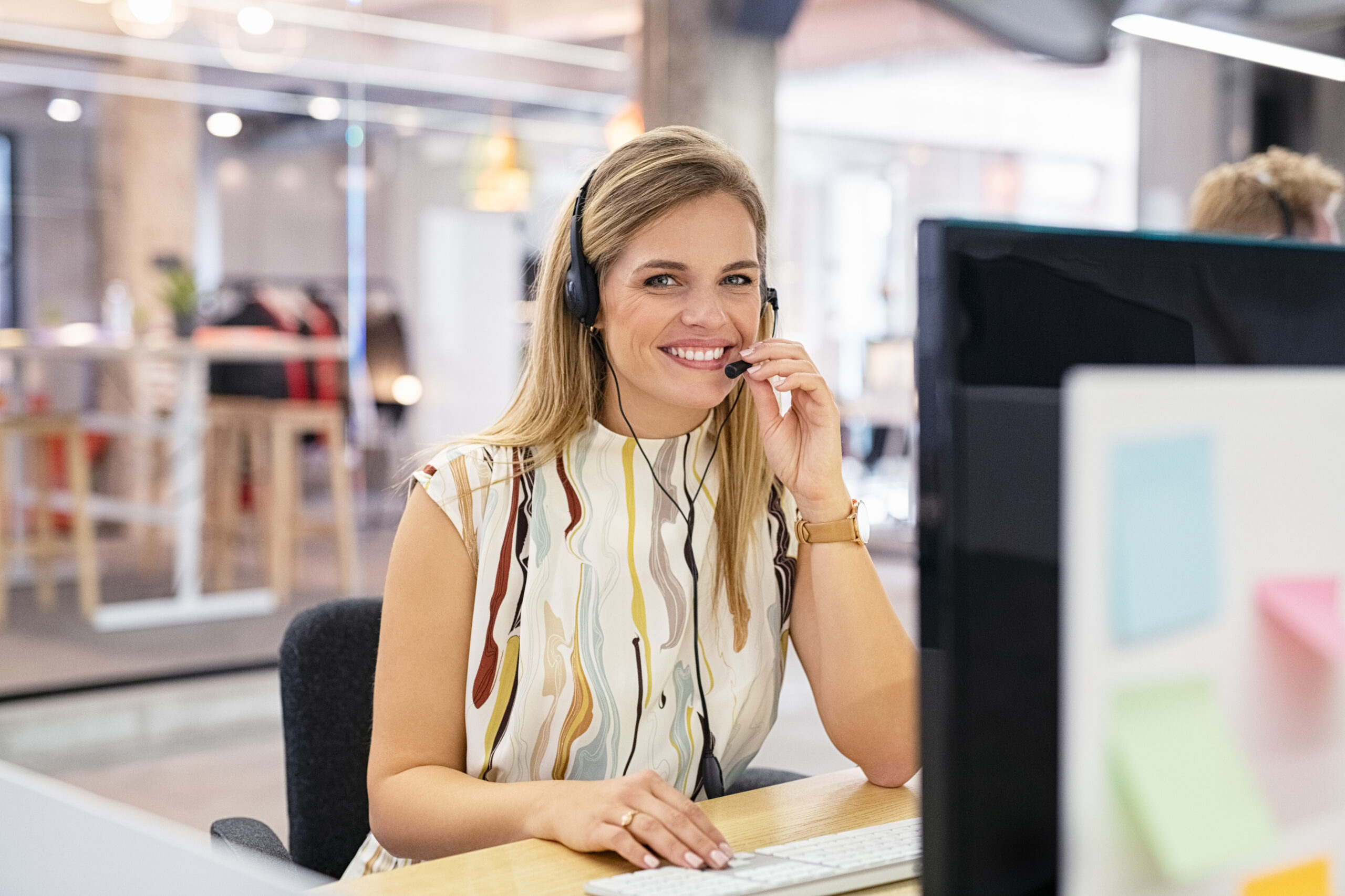 Smiling woman working as customer support operator with headset in a call center. Portrait of happy sales agent sitting at desk in modern office and looking at camera. Customer care and support service rapresentative.