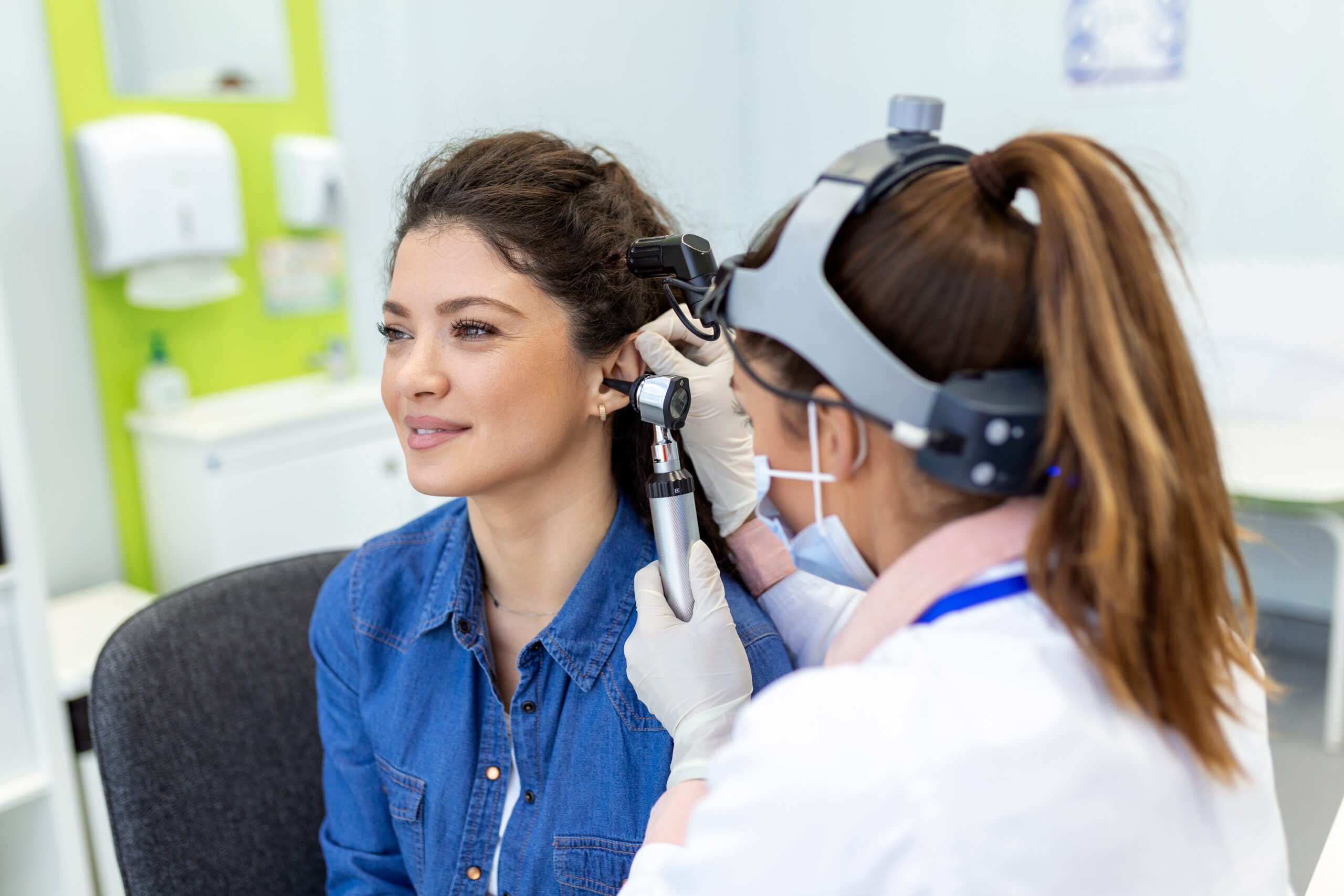 Hearing exam. Otolaryngologist doctor checking woman's ear using otoscope or auriscope at medical clinic. Otorhinolaryngologist pulling ear with hand and looking at it with otoscope closeup.