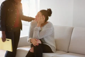 A woman sitting on a sofa with a concerned expression while being comforted by another person—representing mental health challenges linked to hearing loss
